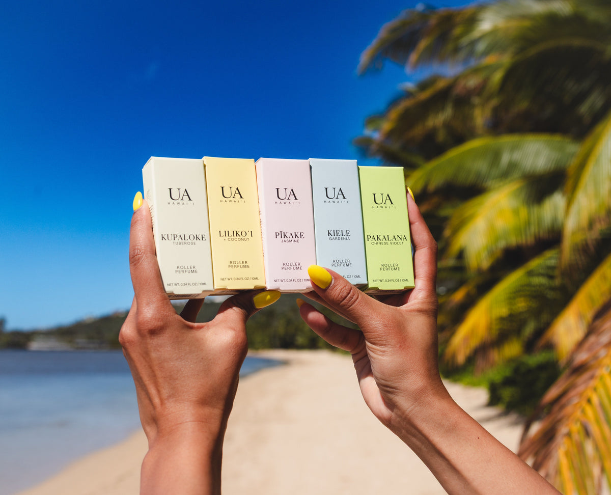 Hands holding Ua products on a beach with palm trees and blue sky