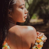 Woman with island background rubbing 'Iliahi Sandalwood Dry Oil on shoulder
